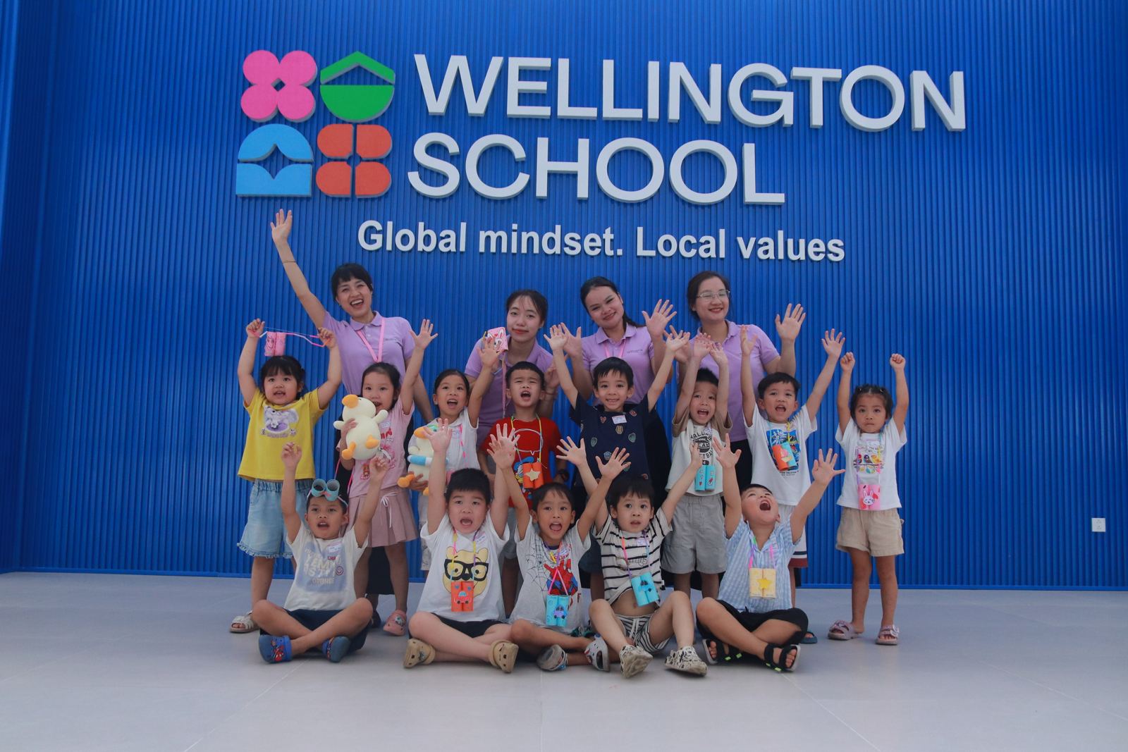 Học sinh và giáo viên Tiền Tiểu học Wellington chụp ảnh trước logo trường